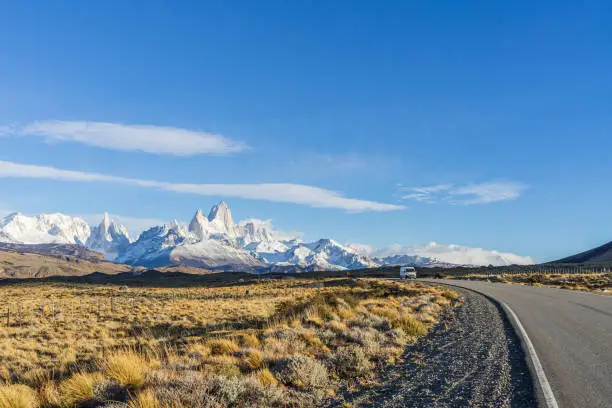 Beautiful asphalt road Route 40 with background of Fitz Roy and Cerro Torre peak snow mountain in the morning blue sky with golden yellow grass in autumn, El Chalten, south Patagonia, Argentina.