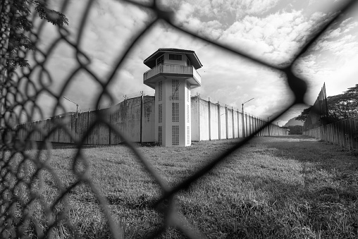 Prison watchtower protected by wire of prison fence.White prison wall and guard tower with coiled barbed wire.Criminal justice imprisonment concept