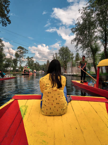 Young woman sitting on bow of traditional Xochimilco boat Xochimilco, Mexico City, June 25, 2019 - Young latin woman sitting on the bow of traditional Xochimilco boat during the tour. trajinera stock pictures, royalty-free photos & images