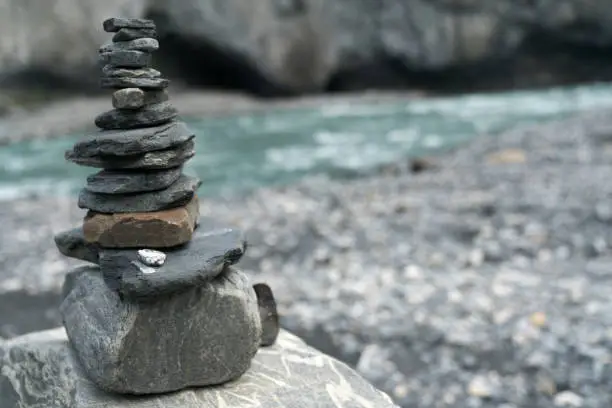 A rock cairn up close with a turquoise mountain river in the background