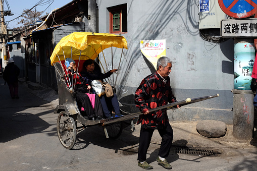 Beijing, China - April 3, 2014: A pedicab driver carries tourists in a Hutong alley.