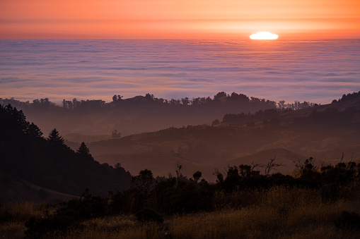 Sun setting over a sea of clouds; layered hills and valleys visible in the foreground; Santa Cruz mountains, San Francisco Bay Area, California