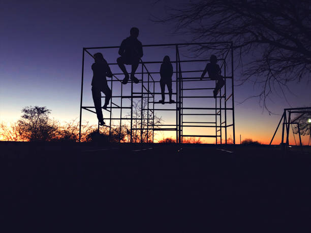 Silhouette of 4 teenage and young children on a playground jungle gym tower at dawn in Namibia Africa