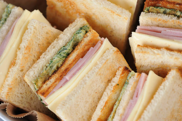 istock White bread sandwiches occupy the entire frame space. Square-shaped sandwiches stuffed with ham, cheese and scrambled eggs with spinach. 1165460410