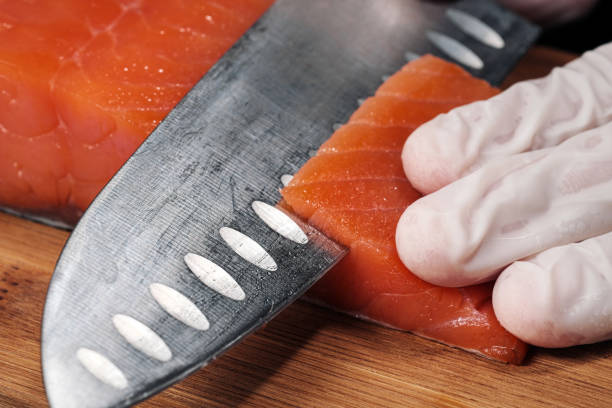 le mani cucinano da vicino. lo chef taglia con un coltello un pesce rosso, salmone affumicato su un tagliere di legno. - japanese cuisine temaki sashimi sushi foto e immagini stock