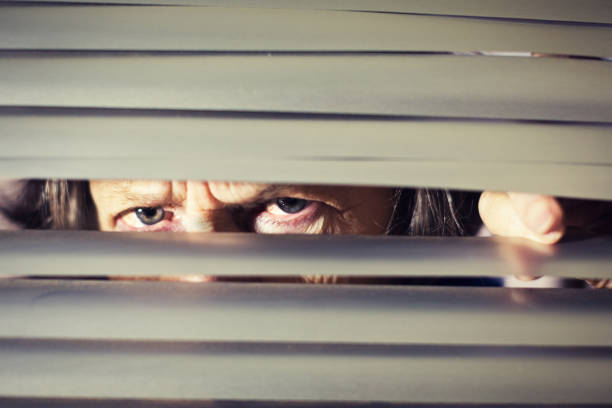 istock Senior woman frowns, peering through venetian blind 1165463679