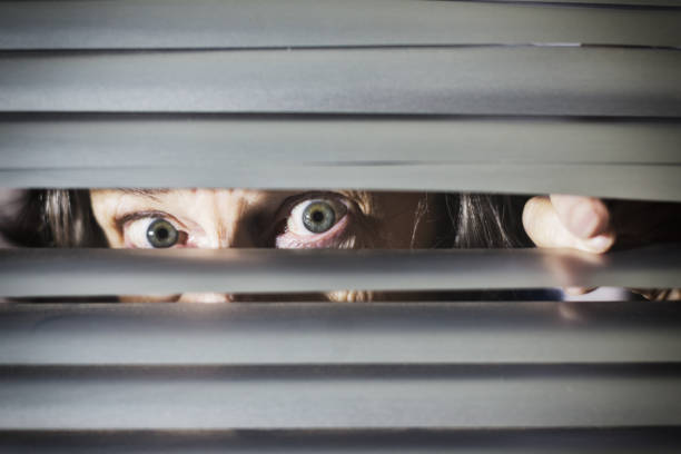 istock Alarmed senior woman peering through venetian blinds 1165463942