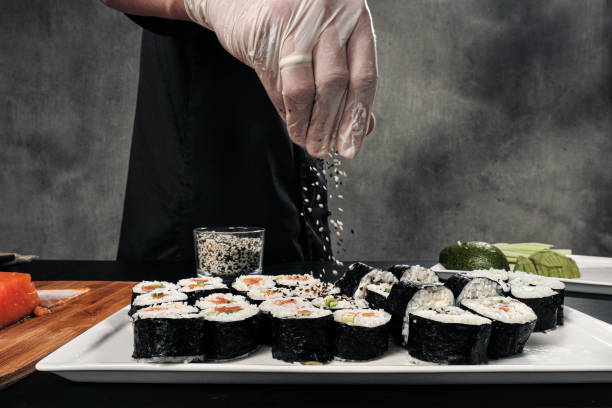le mani di cook sono in primo ci sono. uno chef maschio fa sushi e panini da riso, pesce rosso e avocado. guanti bianchi. - temaki food sushi salmon foto e immagini stock