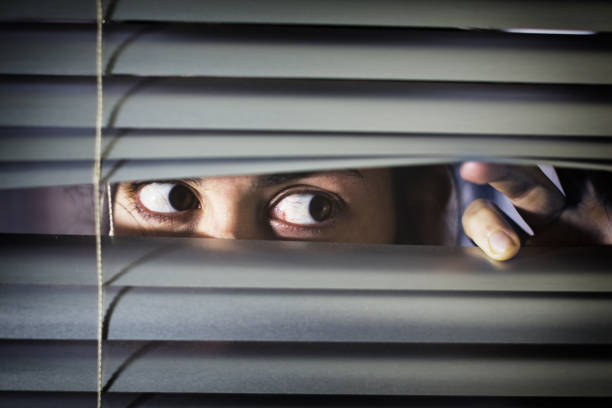 istock Anxious, wide-eyed young brunette peeps sideways through blinds 1165464347