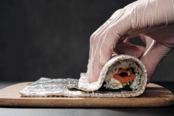 le mani di cook da vicino. uno chef maschio produce sushi e panini da riso, pesce rosso e avocado. guanti bianchi. - temaki food sushi salmon foto e immagini stock