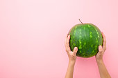 Young woman hands holding one green watermelon on light pastel pink table. Closeup. Empty place for text, quote or sayings. Top view.