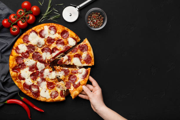 istock Woman taking slice of pepperoni pizza on black table 1165464578