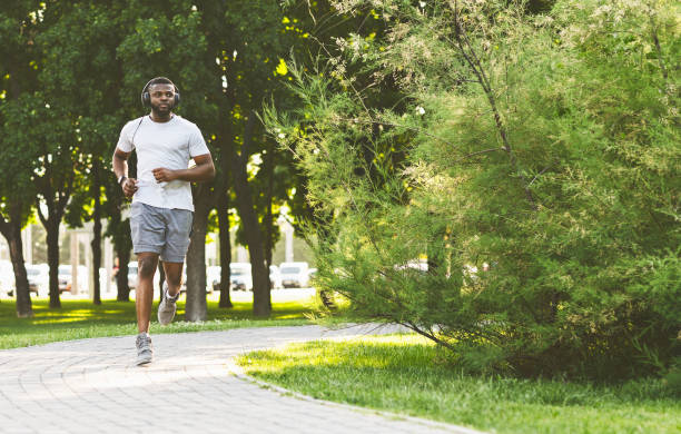 istock Sporty afro guy with headset is running in the park 1165465699
