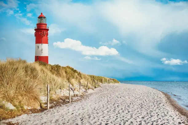 Lighthouse on the beach of an island, on the coast behind and on dune with beach sand and water by the sea. blue sky with white clouds with space for text