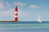 beautiful, old lighthouse and sailboat in bright sunshine, blue sky and blue water