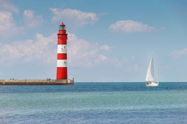 beautiful, old lighthouse and sailboat in bright sunshine, blue sky and blue water stock photo