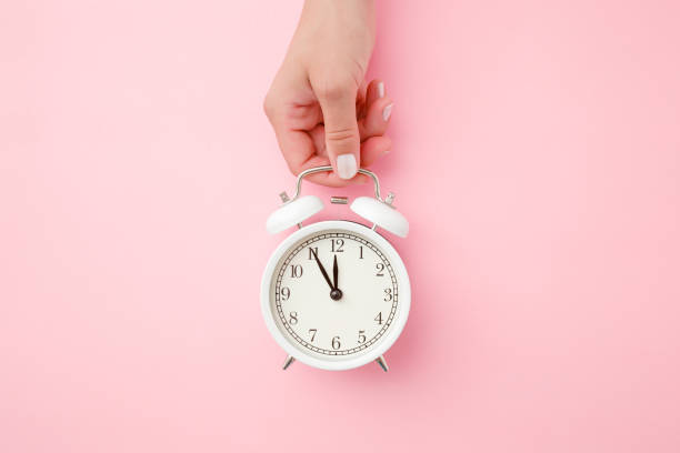 frau hand hält weißen wecker auf hellen pastell rosa hintergrund. zeitkonzept. closeup. ansicht von oben. - number alarm clock clock hand old fashioned stock-fotos und bilder