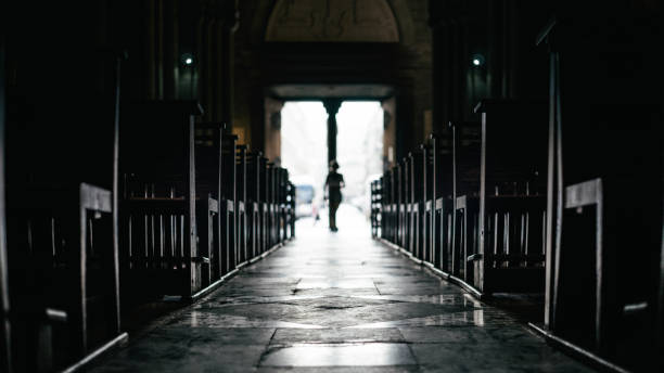 filas de banco dentro de una iglesia silenciosa con transeúnte sin moverse desde la salida - christianity church indoors illuminated fotografías e imágenes de stock