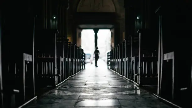 Rows of bench inside a silent church with passerby moving in from exit