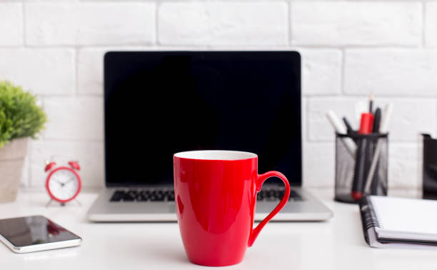 Red cup in front of modern laptop with blank screen