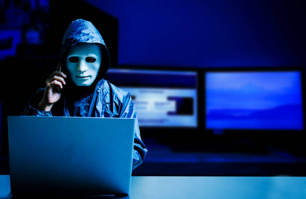 白いマスクとパーカーの匿名のコンピュータハッカー。サイバー攻撃のためのラップトップコンピュータを使用して、携帯電話、データ泥棒、インターネット攻撃、ダークネットとサイバー� - シークレット 人 ストックフォトと画像