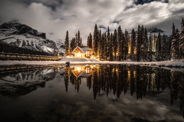 Emerald lake with lodge in Yoho national park, British Columbia, Canada; shot at night with lights on in the chalet reflection on lake 12/19/2018: Emerald lake in Yoho national park, British Columbia, Canada. Shot in winter with deep snow covering lakeshore and pine trees, wood lodge in the photo. yoho national park photos stock pictures, royalty-free photos & images