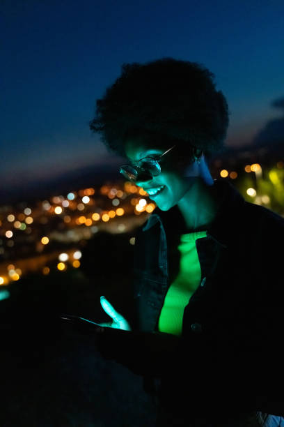 istock Young woman using her mobile phone at night with the city at background 1165473921