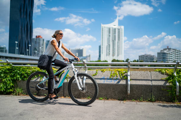 happy businesswoman living sustainable lifestyle cycling on bike to work in city - electric bicycle imagens e fotografias de stock
