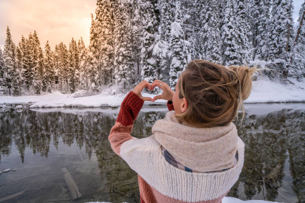 Young woman making heart shape finger frame on snowy pine forest having fun in winter vacations