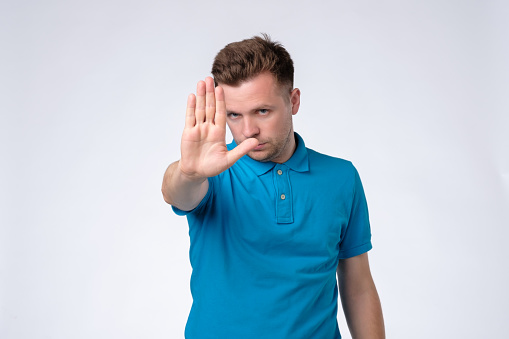 Angry man in blue shirt showing hand. Stop this, stay away from me. Studio shot