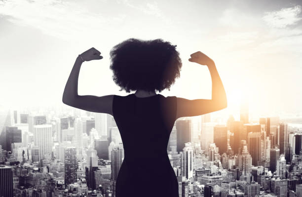 Watch out world! This woman is on her way Rearview shot of an unrecognizable businesswoman standing and flexing her biceps while looking out of her high-rise office flexing muscles stock pictures, royalty-free photos & images