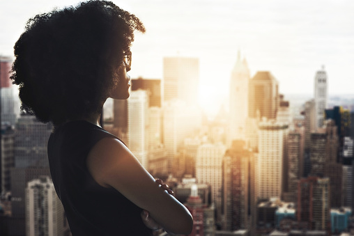 Cropped shot of an attractive young businesswoman standing with her arms crossed and looking out from her high-rise office