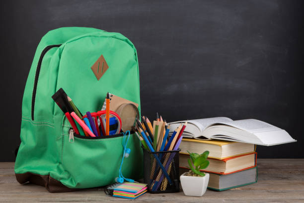 istock Education concept - school backpack with books and other supplies, blackboard background 1165485359