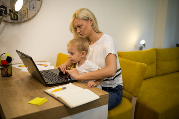 istock Young blonde mother working at home while her son is sitting in her lap 1165485941