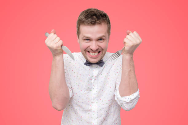 istock Hungry young man holding fork and knife on hand ready to eat, licking lips. 1165486587