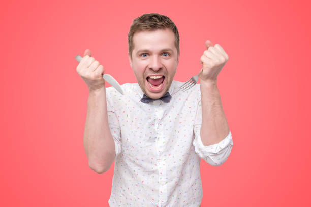 istock Hungry young man holding fork and knife on hand ready to eat, licking lips. 1165486618