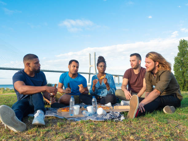 istock Happy people eating pizza and drinking beer during picnic. 1165490640