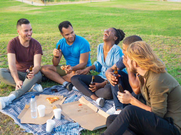 istock Happy smiling people drinking beer and eating pizza during picnic. 1165491669