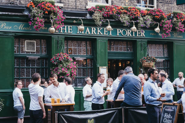 People standing and drinking outside The Market Porter pub in Borough Market, London, UK. London, UK - July 23, 2019: People standing and drinking outside The Market Porter English pub in Borough Market, one of the largest and oldest food markets in London. Selective focus. borough market stock pictures, royalty-free photos & images