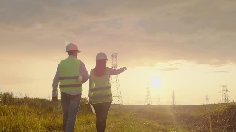 The view from the back: group of engineers at a high-voltage power plant with a tablet and drawings walk and discuss a plan for the supply of electricity to the city.