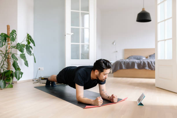 l'homme asiatique emploie la tablette numérique pour pencher la position de planche - home fitness photos et images de collection