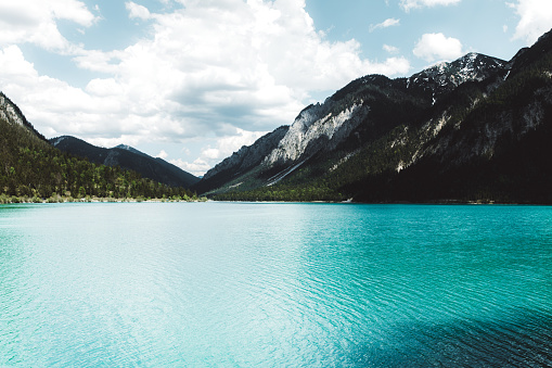 Dramatic view of blue colored lake, Alps mountains and green pine forest in Austria