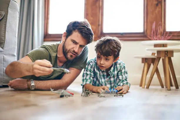 Shot of a little boy and his father playing toy cars at home