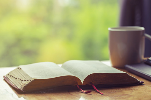 Biblia abierta con una taza de café para la devoción de la mañana en la mesa de madera con luz de ventana photo