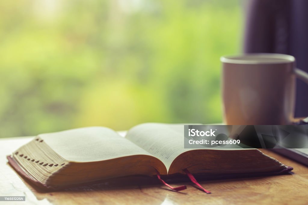 Open bible with a cup of coffee for morning devotion on wooden table with window light Bible Stock Photo