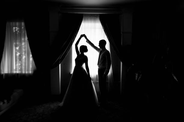 Silhouette of bride and groom by the window. Bride and groom dancing. Newly married couple. Wedding day. The groom holds the bride's hand. The couple dancing the waltz. Wedding dance rehearsal stock photo
