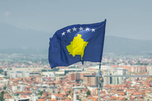 waving flag of Kosovo in front of blurred city waving flag of Kosovo in front of blurred city kosovo stock pictures, royalty-free photos & images