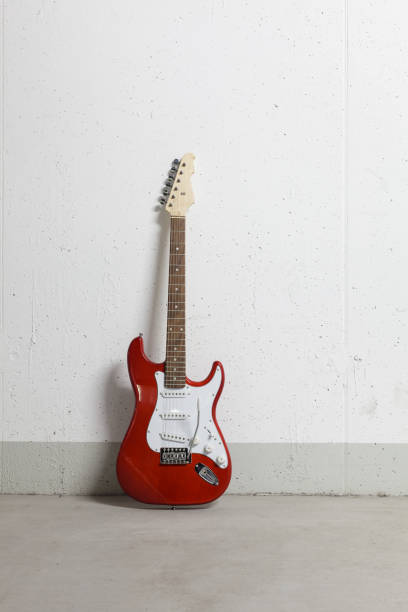 istock Red electric guitar stands on the center against white raw wall 1165518399