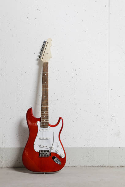 Red electric guitar standing on the left against white raw wall