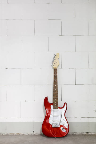 istock Red electric guitar stands against white brick wall background 1165518483